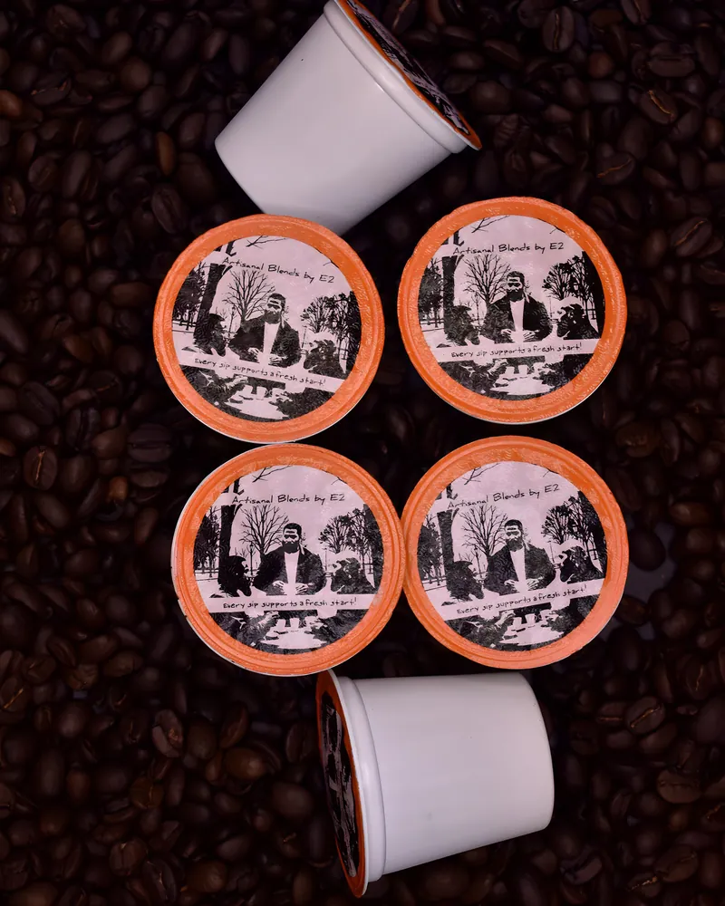 Artisanal Blends by E2 coffee cups with the original artwork printed on the lids, resting on roasted coffee beans